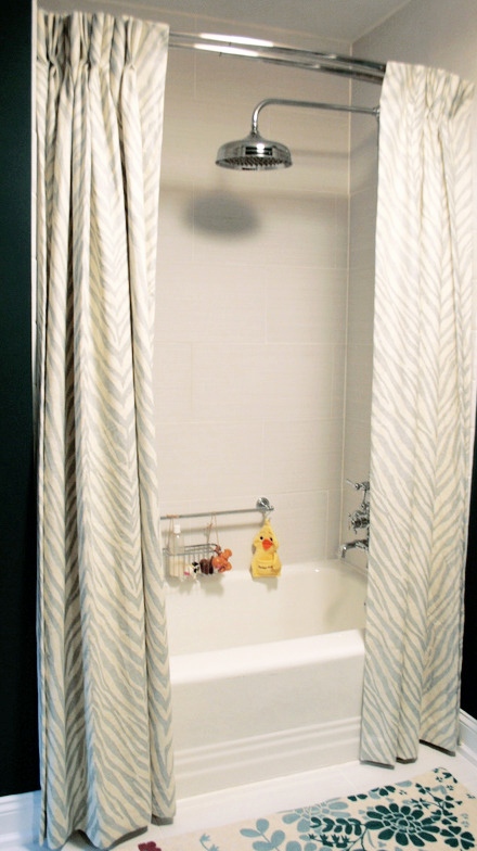 Bathtub with chrome fixtures framed by striped fabric curtains, a rubber duck resting on the tub edge
